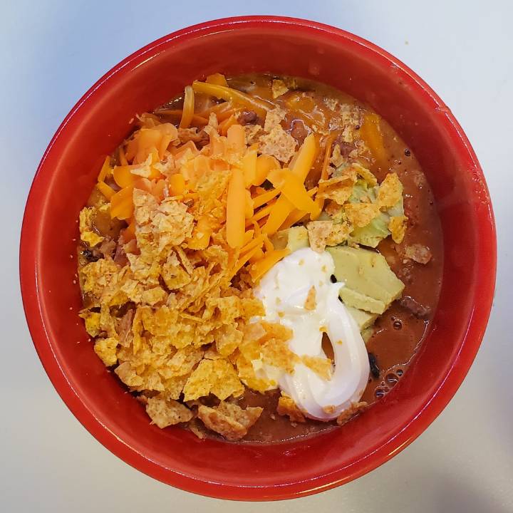 red bowl with taco soup with ranch dressing with shredded cheese, sour cream, avocado and crushed up tortilla chips