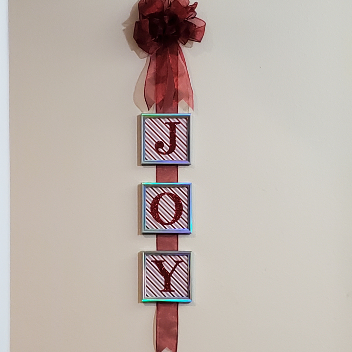 Christmas JOY sign hanging on wall with ribbon and box