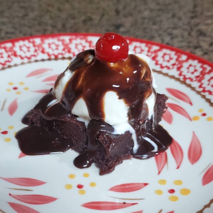 brownie on plate with ice cream, fudge sauce and cherry on top